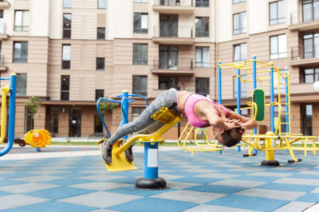 Fit woman trains on exercise machine workout playground near residential building. active lifestyle
