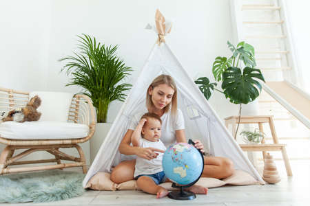 Mom with a little daughter sitting in a wigwam at home, studying the globe. Spend time together. Matyrdom conceptの写真素材