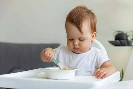 Little child eats while sitting at the children's tableの写真素材