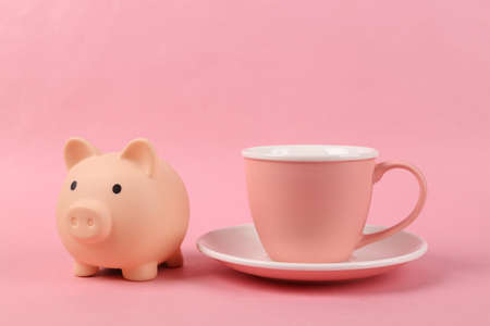 Empty ceramic cup with piggy bank on pink backgroundの写真素材