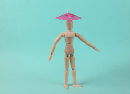 Wooden puppet with umbrella on a blue background. sun protection