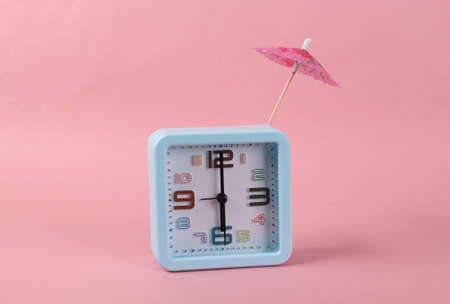 Alarm clock with cocktail umbrella on a pink background. Minimal still life layout