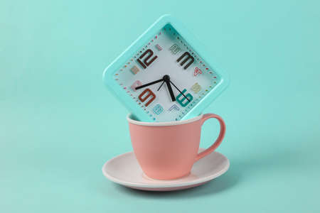 Ceramic cup with alarm clock on blue background