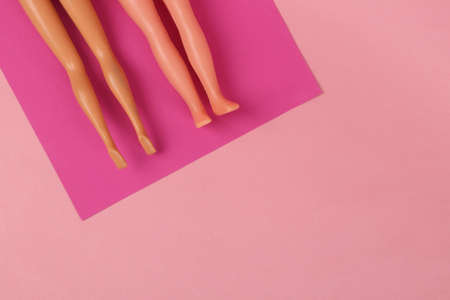 Beach vacation concept. The dolls legs lie on a mat and sunbathe on a pink background. minimal...