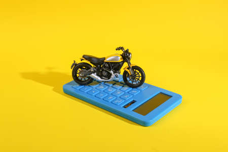 Toy motorcycle with calculator on yellow background. Calculating the cost of fuel costs, or buying a motorcycleの写真素材