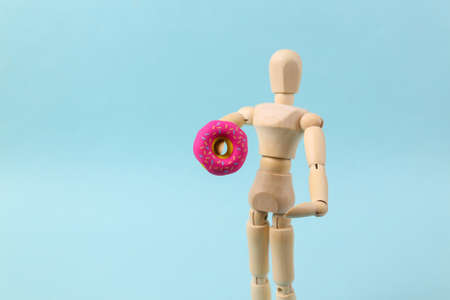 Wooden puppet holding a donut on a blue backgroundの写真素材
