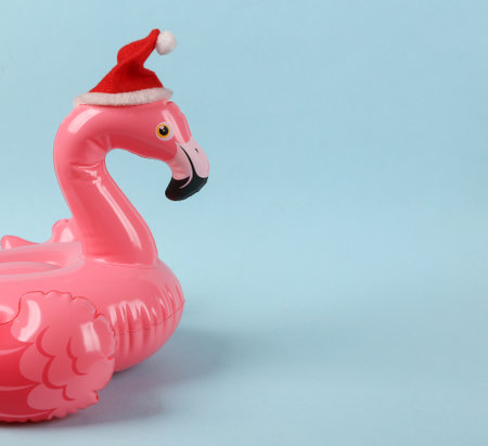 Pink inflatable flamingo with santa hat on a blue background. Minimal christmas layoutの写真素材