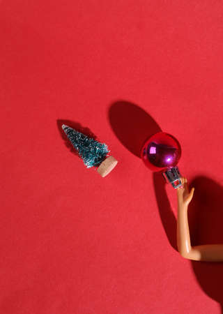 Minimal merry christmas layout. The doll's hand holds a Christmas tree toy ball on a red backgroundの写真素材