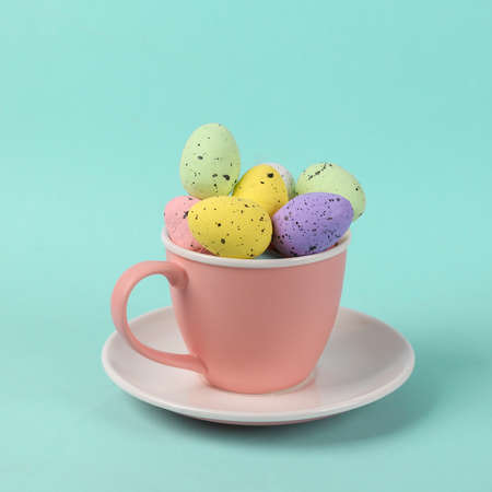 Ceramic cup with colored eggs on blue background. Minimal Easter still life