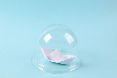Paper sailboat under transparent dome on blue background. protection, isolation concept. minimal layoutの写真素材