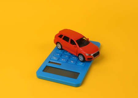 Toy car model with a calculator on a yellow background. Cost calculation, car purchases, fuel consumption, car service costsの写真素材
