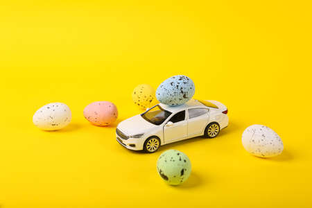 Model of a toy car with Easter eggs on a yellow background. Minimal easter still life