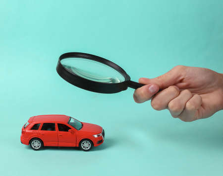 The hand holds a magnifying glass and examines a toy car model through the magnifying glass. car...