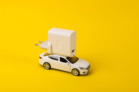 Toy model auto with charger on a yellow background. electric car