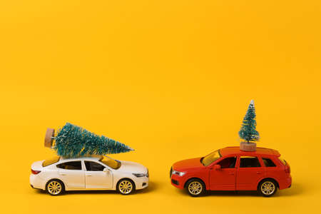 Two Toy cars model with Christmas tree on yellow background. Happy Christmas concept, delivery