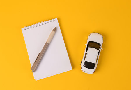 Toy car model with notebook on yellow background. top viewの写真素材