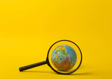 Globe through magnifying glass on yellow backgroundの写真素材
