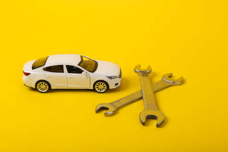 Toy car model with a wrench on a yellow background. Auto service, repair concept.の写真素材