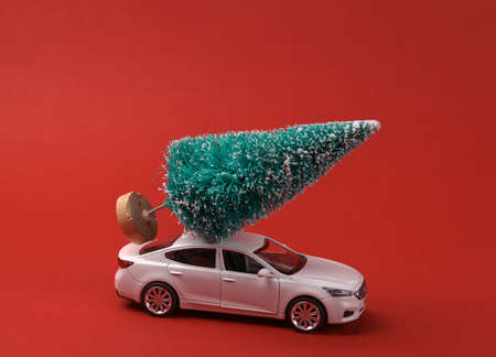 Toy car model with a Christmas tree on red background. Happy Christmas concept, deliveryの写真素材