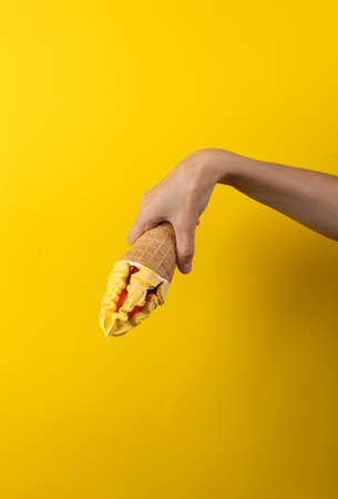 Female hand holds ce cream cone on a yellow background. summer background