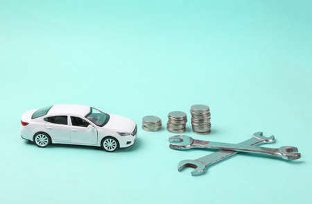 Model of a toy car with wrenches and a stack of coins on a blue background. Auto repair costsの写真素材