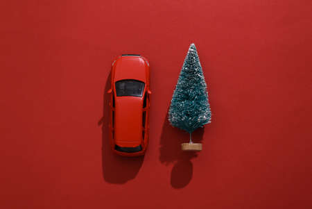 Toy car model with Christmas tree on red background. happy christmas concept