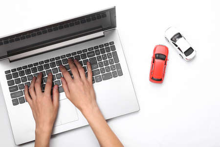 Hands are typing on a laptop keyboard, and toy cars on a white background. Search auto conceptの写真素材