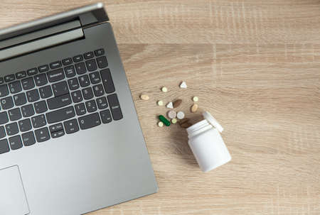 Laptop with bottle of pills on wooden tableの写真素材