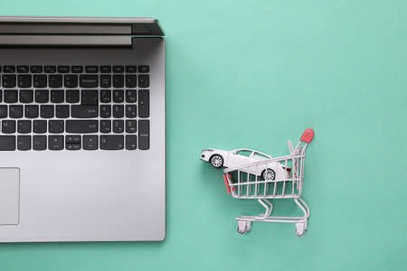 Laptop with a toy car in a shopping trolley on a blue background. Online car purchase. top view