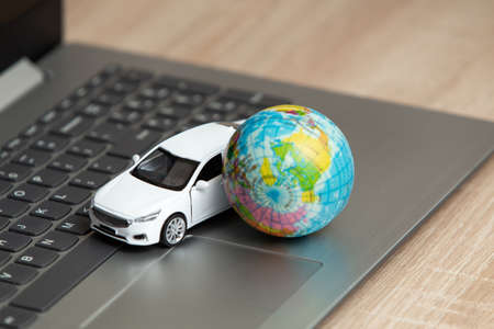 Toy car model with globe on laptop. travel concept