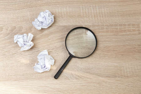 Magnifier with crumpled paper balls on wooden tableの写真素材