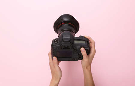 Female hands using professional digital camera on pink background. top view