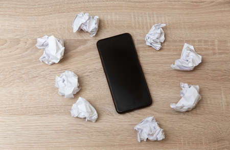 Smartphone with crumpled paper balls on the tableの写真素材
