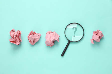 Crumpled pink paper and a magnifying glass with a question mark on blue background.の写真素材