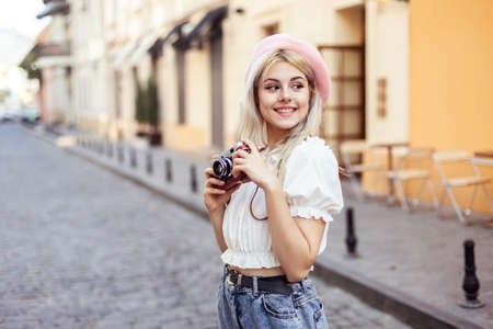 Charming hipster girl in beret with retro camera in city. Travel concept, lifestyle. french styleの写真素材