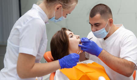 Professional doctor dentist with a woman assistant examines the teeth of a female client in a dental clinic. Visit to the dentist. dental treatmentの写真素材