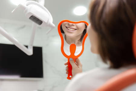 Young girl examines her beautiful smile while sitting in a dental chairの写真素材