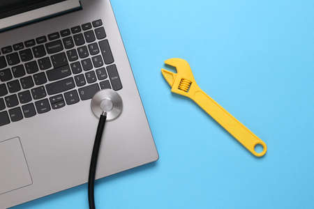 Laptop diagnostics and repair concept. Laptop with stethoscope and wrench on blue background