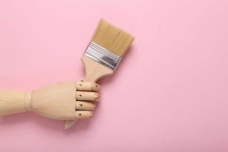 Wooden hand holding Paintbrush on pink background