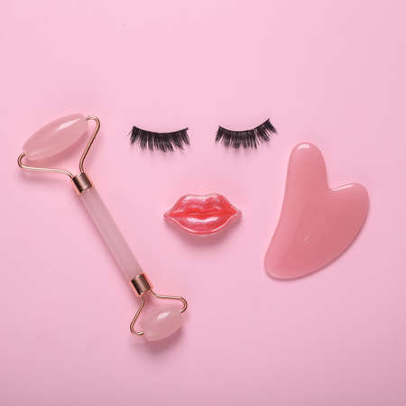 False eyelashes with lips in the shape of a face and facial massage roller on pink background. Beauty minimal still life. flat layの写真素材