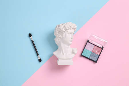 Minimal beauty still life. Plaster bust of david with Eyeshadow palette on blue pink pastel backgroundの写真素材