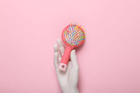 Plastic hand holding hairbrush on pink backgroundの写真素材