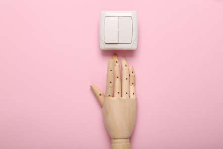 Wooden hand presses on light switch on pink background