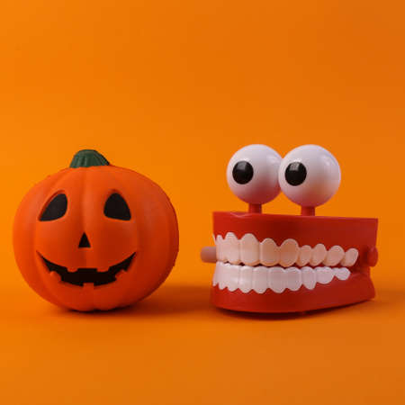 Clockwork jaw with pumpkin jack lantern head on orange background. Halloween decorations. Minimal...