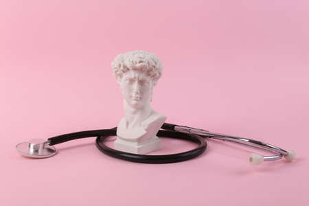 Stethoscope with antique bust of David on a pink background. medical composition. Minimal still lifeの写真素材