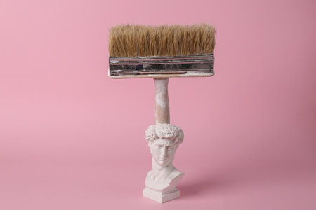 Antique bust of David with paint brush on pink background. concept pop. Minimal still life.