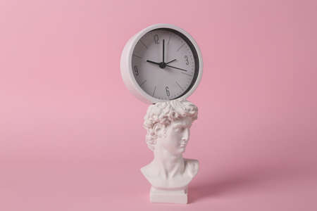 Antique David bust with clock on pink background. concept pop. Minimal still life. creative ideasの写真素材