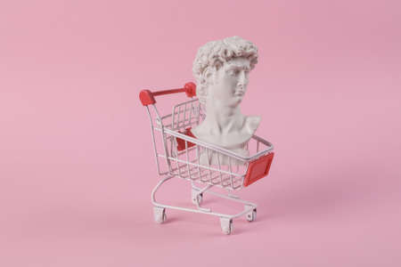 Antique bust of David with shopping trolley on a pink background. concept pop. Minimal shopping still life. creative ideasの写真素材
