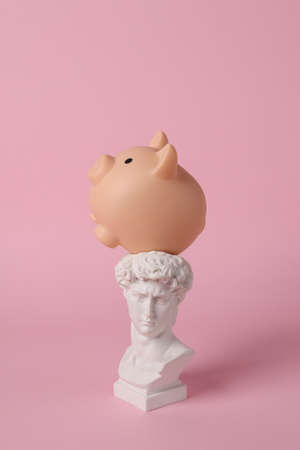 Antique bust of David with piggy bank on pink background. concept pop. Minimal still life.の写真素材