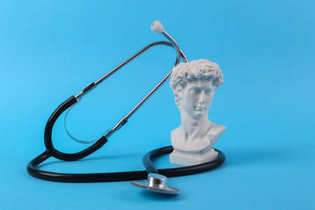 Stethoscope with antique bust of David on blue background. medical composition. Minimal still lifeの写真素材